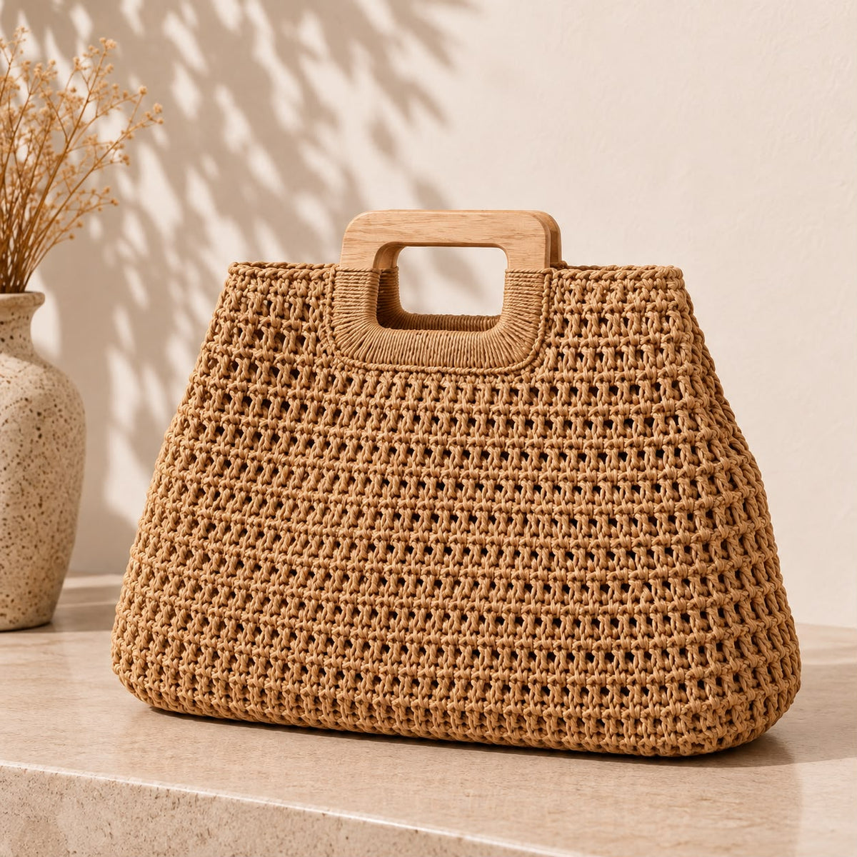 Bolso tejido en fibra natural con asa de madera junto a un jarrón